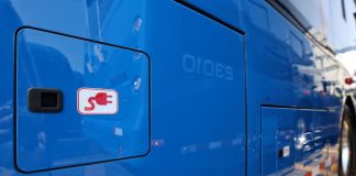 Blue electric municipal-style bus with an icon of an electric plug on the bus.