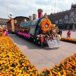 Megaofrenda in Mexico City's Zocalo square, of a parade float made to look like a steam locomotive, decorated in papel picada, Mexican marigolds and a larger-than-life figure of a Mexican revolutionary holding a gun and wearing a straw sombrero.