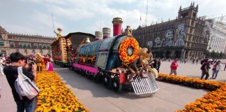 Megaofrenda in Mexico City's Zocalo square, of a parade float made to look like a steam locomotive, decorated in papel picada, Mexican marigolds and a larger-than-life figure of a Mexican revolutionary holding a gun and wearing a straw sombrero.