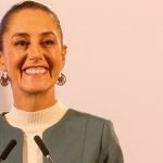 Claudia Sheinbaum staring into the camera at a press conference and smiling.