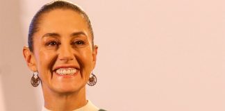 Claudia Sheinbaum staring into the camera at a press conference and smiling.