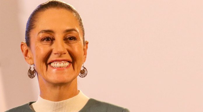 Claudia Sheinbaum staring into the camera at a press conference and smiling.