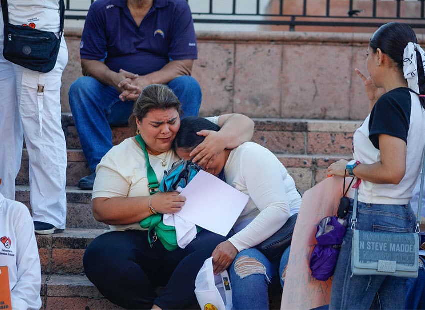 Woman sitting on stone stairs has her arm around the head of another woman who appears to be struck with grief. Both are participants in a march in Culiacan, Sinaloa, to demand that authorities put an end to the wave of cartel violence currently killing and kidnapping hundreds of residents.