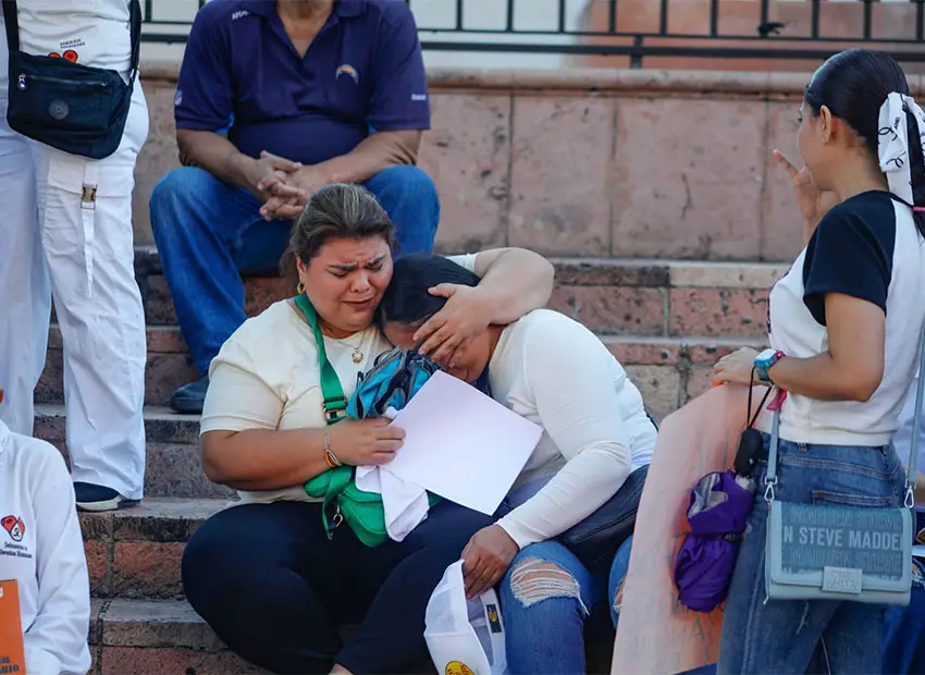 Woman sitting on stone stairs has her arm around the head of another woman who appears to be struck with grief. Both are participants in a march in Culiacan, Sinaloa, to demand that authorities put an end to the wave of cartel violence currently killing and kidnapping hundreds of residents.