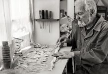 Black and white photo of artist Alan Glass laying out the skeleton of some sort of long fish-like animal in his art studio.