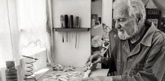 Black and white photo of artist Alan Glass laying out the skeleton of some sort of long fish-like animal in his art studio.
