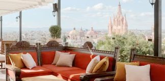 Luxurious sofas made of carved dark wood and with orange cushions and white and beige pillows on a rooftop terrace looking at skyline of San Miguel de Allende, Guanajuato, Mexico.