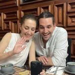 Claudia Sheinbaum and her stepson Rodrigo Ímaz Alarcón, sitting in a restaurant at a table with coffee cups and looking at something on a cell phone