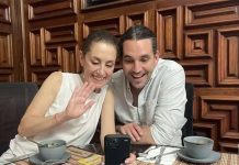 Claudia Sheinbaum and her stepson Rodrigo Ímaz Alarcón, sitting in a restaurant at a table with coffee cups and looking at something on a cell phone