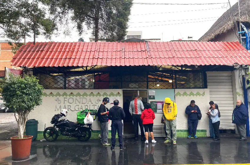 Fachada de la Fonda Margarita, con 8 hombres y mujeres esperando afuera para sentarse