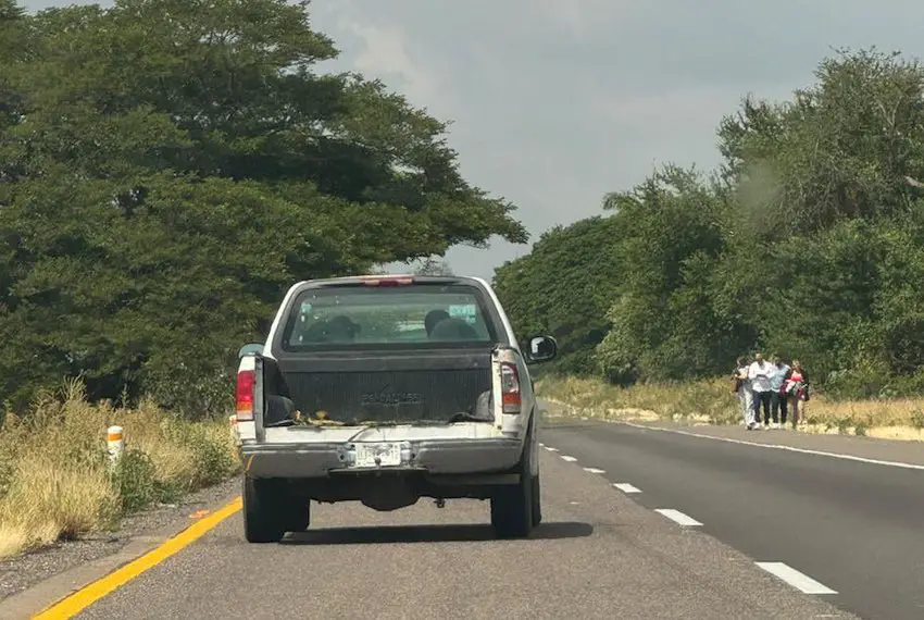 Una camioneta en una carretera de dos carriles en Sinaloa pasando junto a un pequeño grupo de personas que caminaban al costado de la carretera.