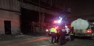 Emergency responders with a water truck at the nighttime scene of an explosion at a Tlaxcala steel mill