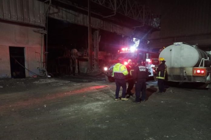 Emergency responders with a water truck at the nighttime scene of an explosion at a Tlaxcala steel mill