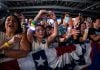 Kamala Harris supporters at a rally in the U.S. A older Latina woman and a young Latina girl are featured in this picture of a crowd behind a red, white and blue barrier. They are cheering and taking photos with their cell phones