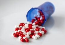 A translucent blue pill bottle with red and white capsules inside spilling out onto an abstract white surface.