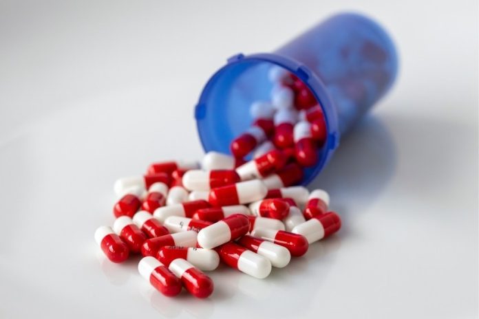 A translucent blue pill bottle with red and white capsules inside spilling out onto an abstract white surface.