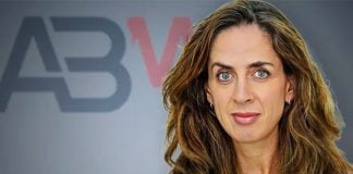 Woman with long wavy light brown hair staring into the camera, posing in front of a wall that has the letters ABM on it.