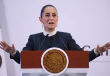 Claudia Sheinbaum at her press conference podium with her hands up and palms facing the floor in a gesture telling people to calm down.