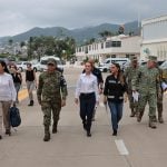 Mexico's President Claudia Sheinbaum in a white Oxford shirt and black pants, walking down a street in Guerrero, Mexico, with other government functionaries, including several in military fatigues.