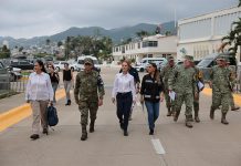 Mexico's President Claudia Sheinbaum in a white Oxford shirt and black pants, walking down a street in Guerrero, Mexico, with other government functionaries, including several in military fatigues.