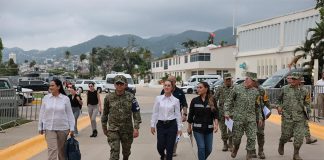 Mexico's President Claudia Sheinbaum in a white Oxford shirt and black pants, walking down a street in Guerrero, Mexico, with other government functionaries, including several in military fatigues.