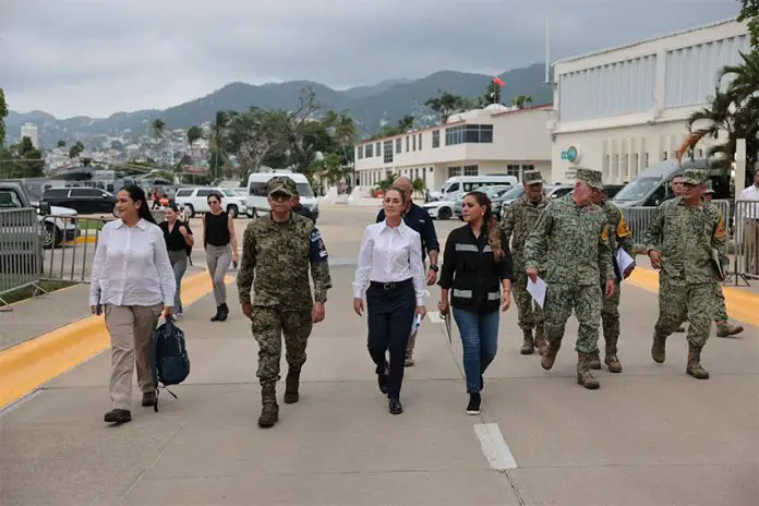 Mexico's President Claudia Sheinbaum in a white Oxford shirt and black pants, walking down a street in Guerrero, Mexico, with other government functionaries, including several in military fatigues.