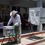 Mexican man putting a ballot into a voting box at a polling station