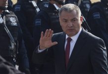 Genaro Garcia Luna in 2011 waving at the camera while Mexico's Federal Police stand at attention in rows to his right