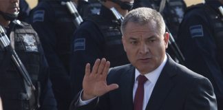 Genaro Garcia Luna in 2011 waving at the camera while Mexico's Federal Police stand at attention in rows to his right