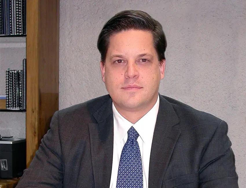 Mexican Supreme Court Justice Alfredo Gutiérrez Ortiz Mena in a suit and tie posing for a photo in an office with a bookcase with binders in the background