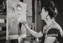 Black and white photo of Frida Kahlo looking at a painting she's working on of a portrait of her father, Guillermo Kahlo.