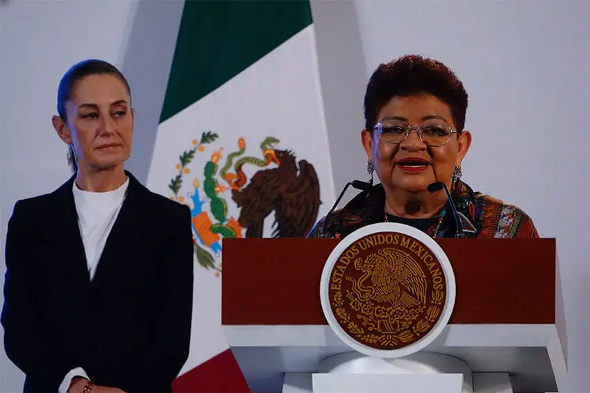 Ernestina Godoy, asesora legal del presidente, habla en un podio con la presidenta Sheinbaum detrás de ella.