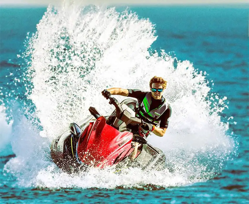 A man sprays water behind him as he rides a red Kawasaki Jet Ski