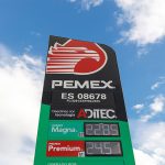 A Pemex gas station sign against a blue sky dotted with clouds