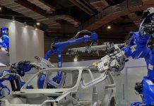 Shandong Golden Empire manufacturing demonstration with a white car frame in a conference hall and blue robotic arms on either side of the frame manipulating auto parts