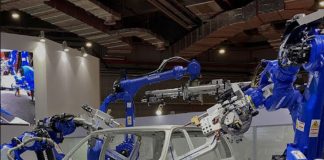 Shandong Golden Empire manufacturing demonstration with a white car frame in a conference hall and blue robotic arms on either side of the frame manipulating auto parts