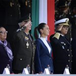 Sheinbaum stands in front of a tri-colored banner, as military officials salute at her side.