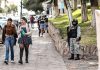 Young women walk down a sidewalk while a member of the National Guard stands guard, illustrating the level of perceived insecurity in Mexican cities