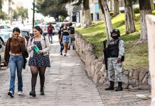 Young women walk down a sidewalk while a member of the National Guard stands guard, illustrating the level of perceived insecurity in Mexican cities