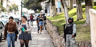 Young women walk down a sidewalk while a member of the National Guard stands guard, illustrating the level of perceived insecurity in Mexican cities