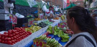 A woman looks at fruit and vegetables in a Mexican market, with the prices marked