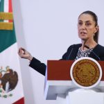 President Claudia Sheinbaum behind a podium at a press conference gesturing with one hand as she talks to reporters.