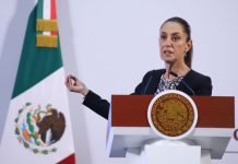 President Claudia Sheinbaum behind a podium at a press conference gesturing with one hand as she talks to reporters.