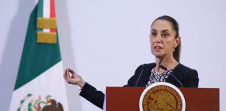 President Claudia Sheinbaum behind a podium at a press conference gesturing with one hand as she talks to reporters.