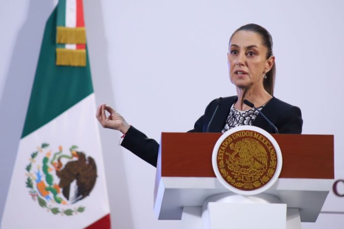 President Claudia Sheinbaum behind a podium at a press conference gesturing with one hand as she talks to reporters.