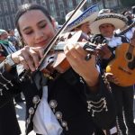 A woman in a mariachi outfit plays the violin, surrounded by other mariachi musicians as they attempt to break the Guinness World Record for largest performance