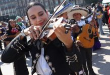 A woman in a mariachi outfit plays the violin, surrounded by other mariachi musicians as they attempt to break the Guinness World Record for largest performance