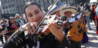 A woman in a mariachi outfit plays the violin, surrounded by other mariachi musicians as they attempt to break the Guinness World Record for largest performance