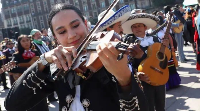 A woman in a mariachi outfit plays the violin, surrounded by other mariachi musicians as they attempt to break the Guinness World Record for largest performance