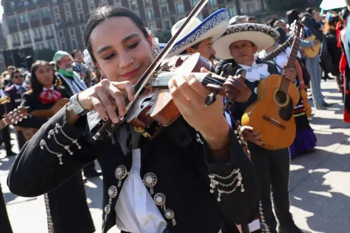 A woman in a mariachi outfit plays the violin, surrounded by other mariachi musicians as they attempt to break the Guinness World Record for largest performance